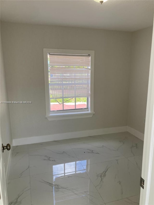 unfurnished room featuring marble finish floor and baseboards