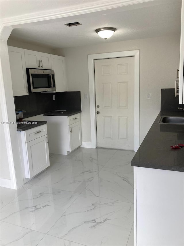 kitchen featuring a sink, stainless steel microwave, marble finish floor, and white cabinets