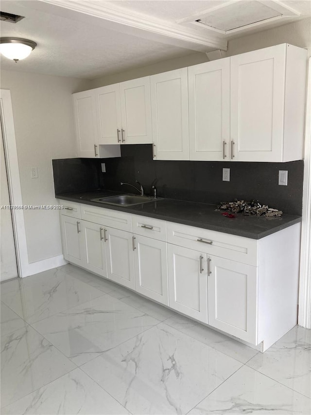kitchen featuring tasteful backsplash, white cabinetry, dark countertops, marble finish floor, and a sink