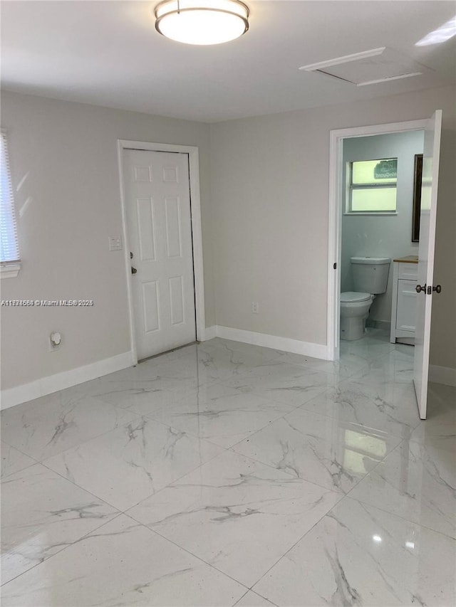 unfurnished room featuring marble finish floor, baseboards, and attic access