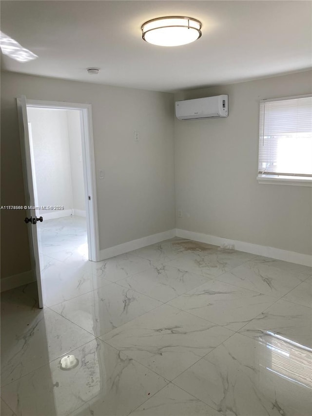 empty room with marble finish floor, an AC wall unit, and baseboards