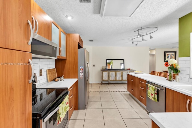 kitchen with brown cabinets, appliances with stainless steel finishes, decorative backsplash, and light countertops