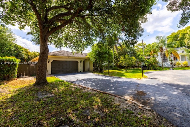 view of front of house featuring an attached garage, a front lawn, a tile roof, stucco siding, and driveway