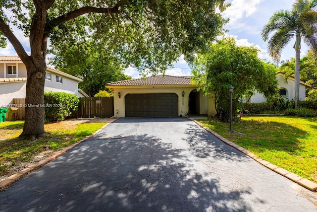 view of front facade with fence, a tile roof, aphalt driveway, a garage, and stucco siding