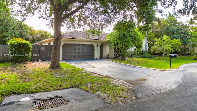 single story home with a garage, a front lawn, aphalt driveway, fence, and stucco siding