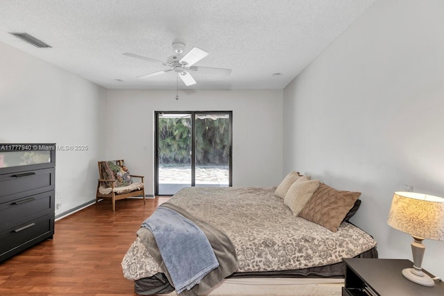 bedroom featuring dark wood-style flooring, a textured ceiling, access to exterior, a ceiling fan, and visible vents