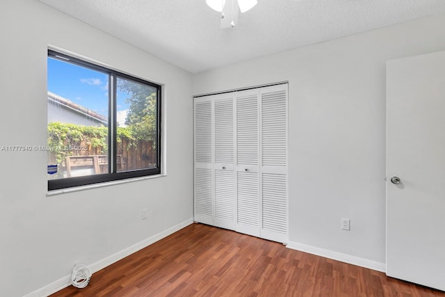 unfurnished bedroom with a textured ceiling, a ceiling fan, baseboards, wood finished floors, and a closet