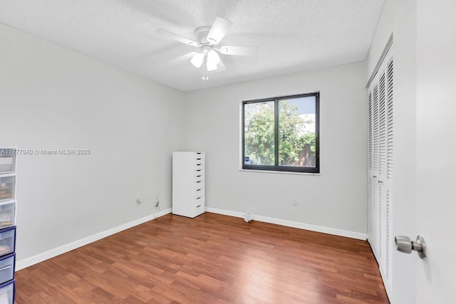 unfurnished bedroom with ceiling fan, a textured ceiling, baseboards, wood finished floors, and a closet