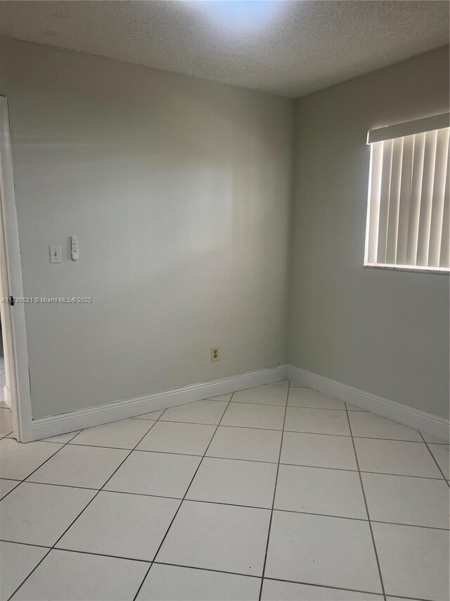 unfurnished room featuring a textured ceiling, light tile patterned floors, and baseboards