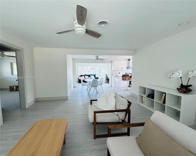 living area featuring light wood-type flooring, visible vents, a ceiling fan, and baseboards