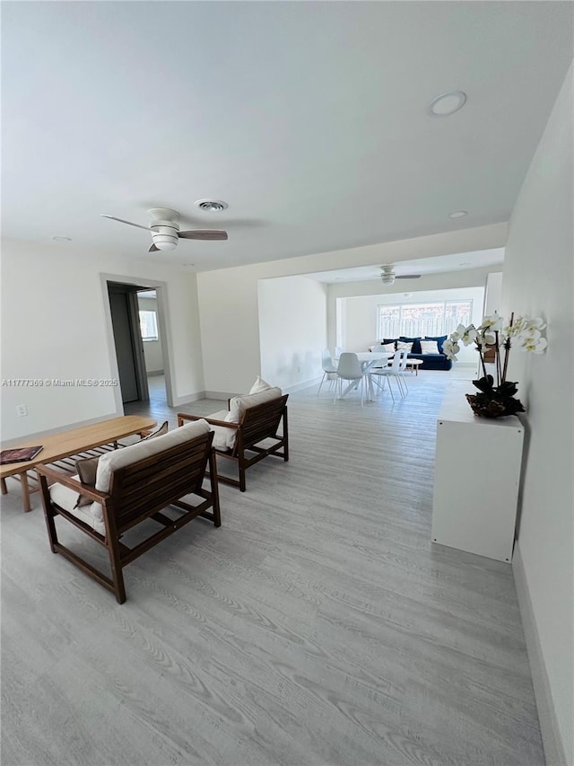 living room with light wood-style floors, visible vents, a ceiling fan, and baseboards
