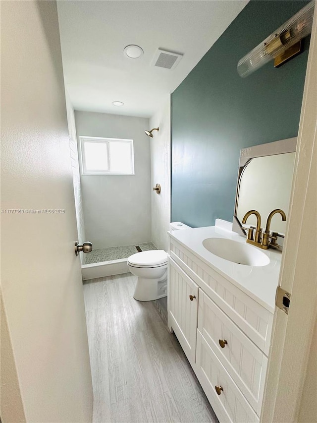 bathroom featuring wood finished floors, a stall shower, vanity, toilet, and visible vents