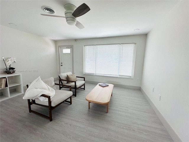 living area with light wood-type flooring, visible vents, baseboards, and ceiling fan