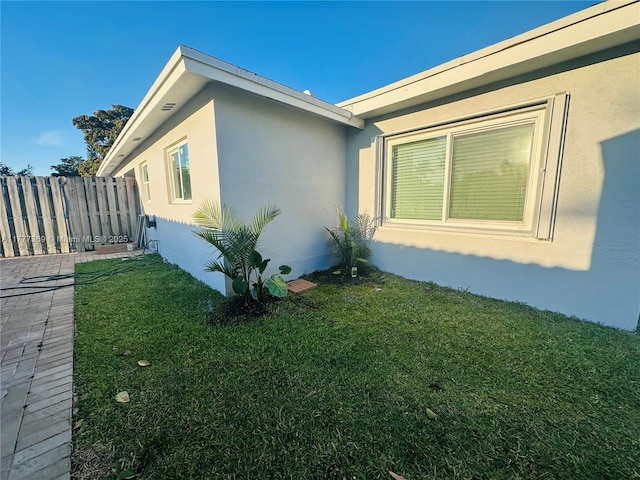view of side of home featuring fence, a yard, and stucco siding
