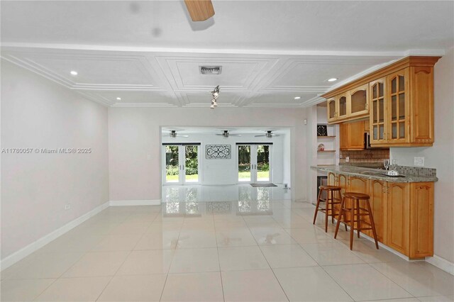 kitchen with visible vents, glass insert cabinets, a ceiling fan, a kitchen breakfast bar, and brown cabinets