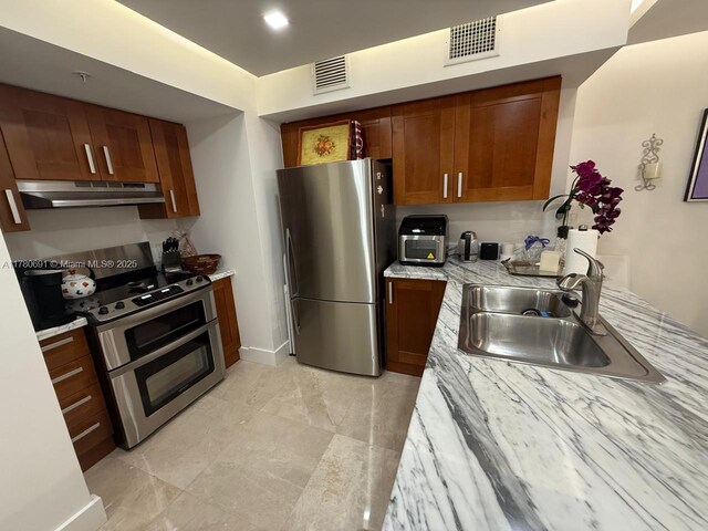 9499 Collins Ave Unit 411, Surfside, FL 33154 - kitchen with appliances with stainless steel finishes, under cabinet range hood, brown cabinets, and light stone counters