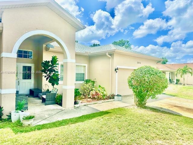 3315 18 W, Lehigh Acres, FL 33971 - view of side of home with a yard, driveway, a garage, and stucco siding