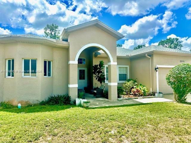 3315 18 W, Lehigh Acres, FL 33971 - property entrance with an attached garage, stucco siding, and a lawn