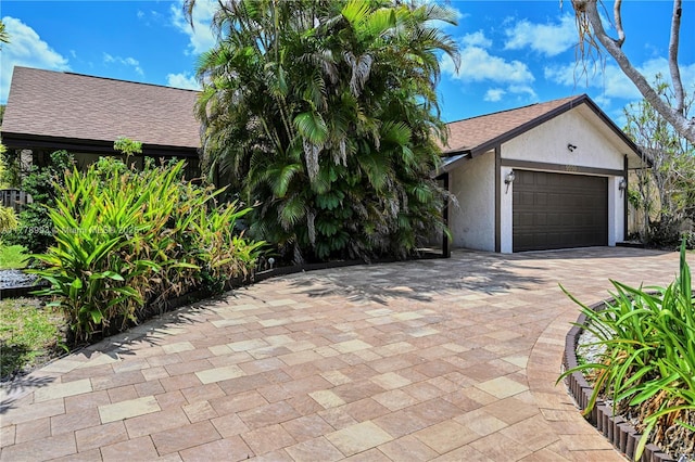 view of front of house with an attached garage, stucco siding, a shingled roof, and driveway