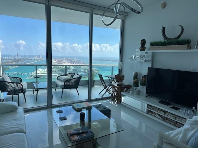 living room featuring expansive windows, a water view, tile patterned floors, and a view of city