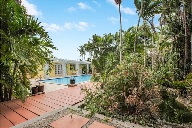 outdoor pool featuring a wooden deck, a pergola, a patio, and french doors