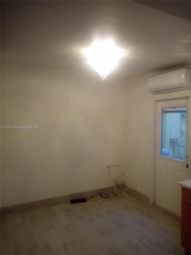 empty room featuring light wood-style flooring, baseboards, and a wall mounted AC