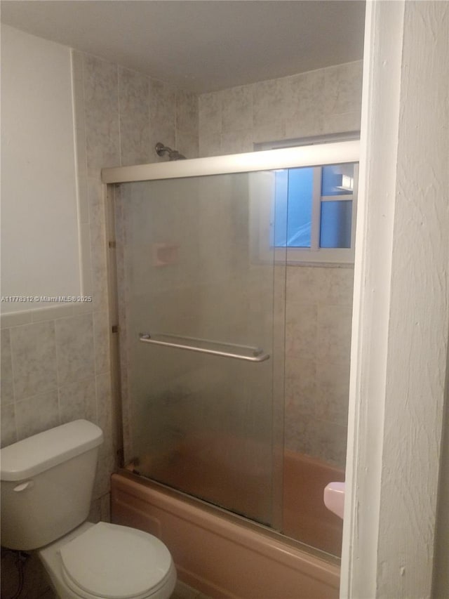 full bathroom with tile walls, toilet, and enclosed tub / shower combo