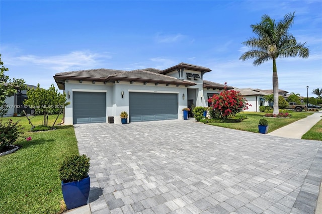 prairie-style house featuring stucco siding, decorative driveway, a front lawn, an attached garage, and a tile roof