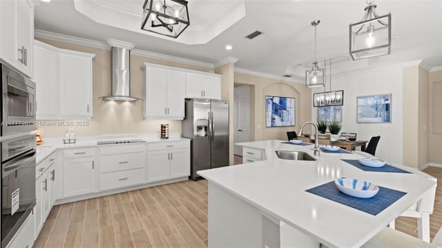 kitchen with an inviting chandelier, a sink, wall chimney exhaust hood, stainless steel appliances, and visible vents