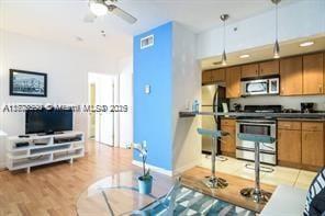 7326 Collins Ave Unit 102, Miami Beach, FL 33141 - kitchen featuring stainless steel appliances, brown cabinetry, light wood-type flooring, ceiling fan, and pendant lighting