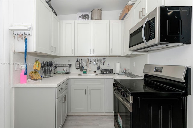 kitchen featuring a sink, light countertops, light wood finished floors, white cabinetry, and stainless steel appliances