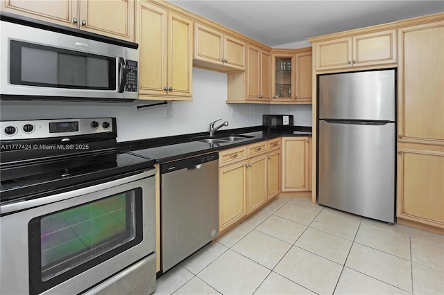 kitchen with light tile patterned floors, light brown cabinets, a sink, dark countertops, and stainless steel appliances