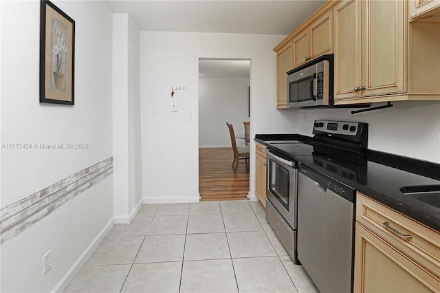 kitchen with light tile patterned floors, light brown cabinetry, dark stone countertops, appliances with stainless steel finishes, and baseboards