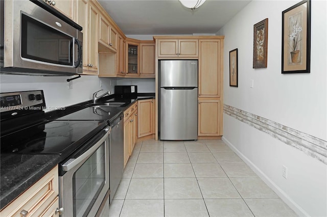 kitchen with light tile patterned floors, glass insert cabinets, a sink, stainless steel appliances, and light brown cabinets
