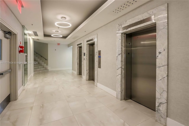 corridor featuring elevator, a tray ceiling, baseboards, and stairway