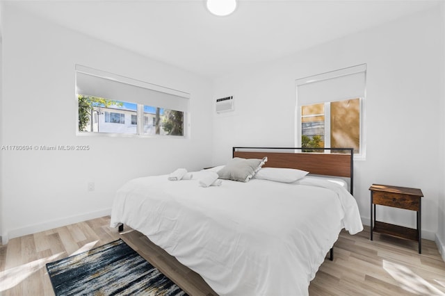 bedroom featuring a wall mounted AC, wood finished floors, and baseboards