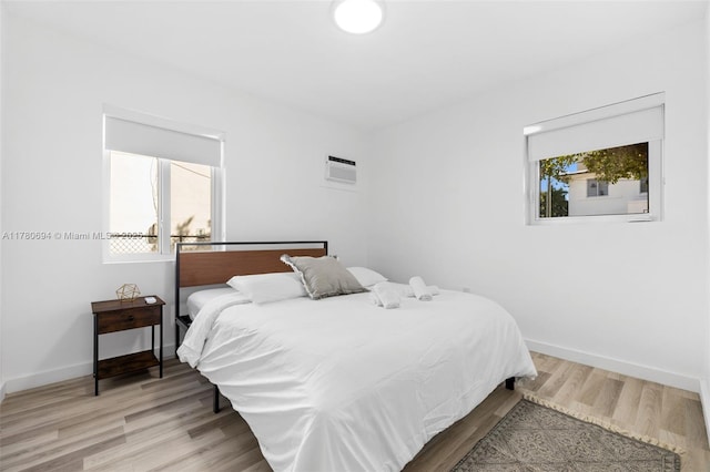 bedroom with an AC wall unit, baseboards, multiple windows, and wood finished floors