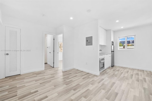 unfurnished living room with electric panel, recessed lighting, light wood-type flooring, and baseboards