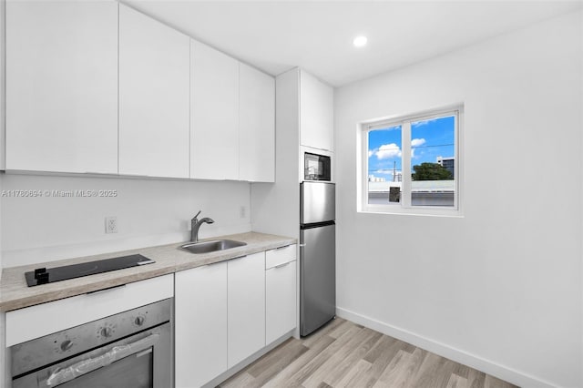 kitchen with a sink, freestanding refrigerator, oven, and white cabinetry