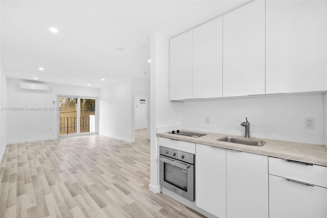 kitchen with an AC wall unit, light countertops, white cabinetry, stainless steel oven, and a sink