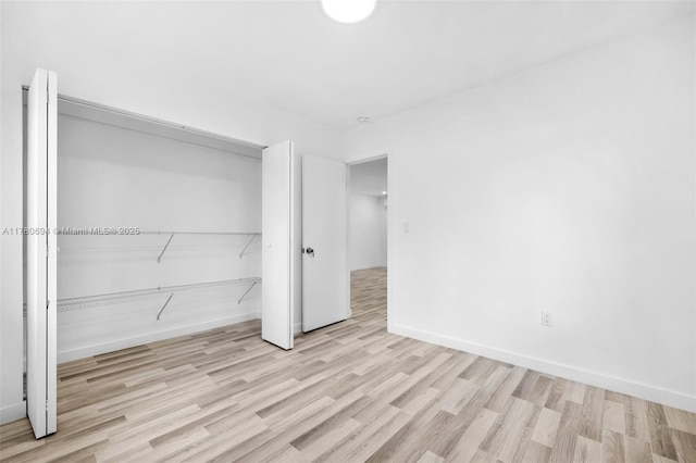 unfurnished bedroom featuring wood finished floors, baseboards, and a closet