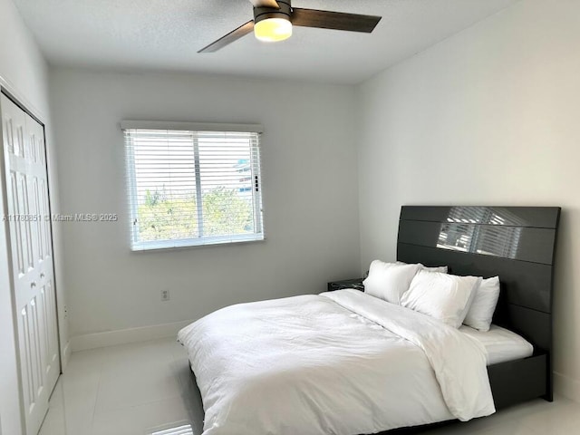bedroom featuring baseboards, a ceiling fan, light tile patterned flooring, and a closet