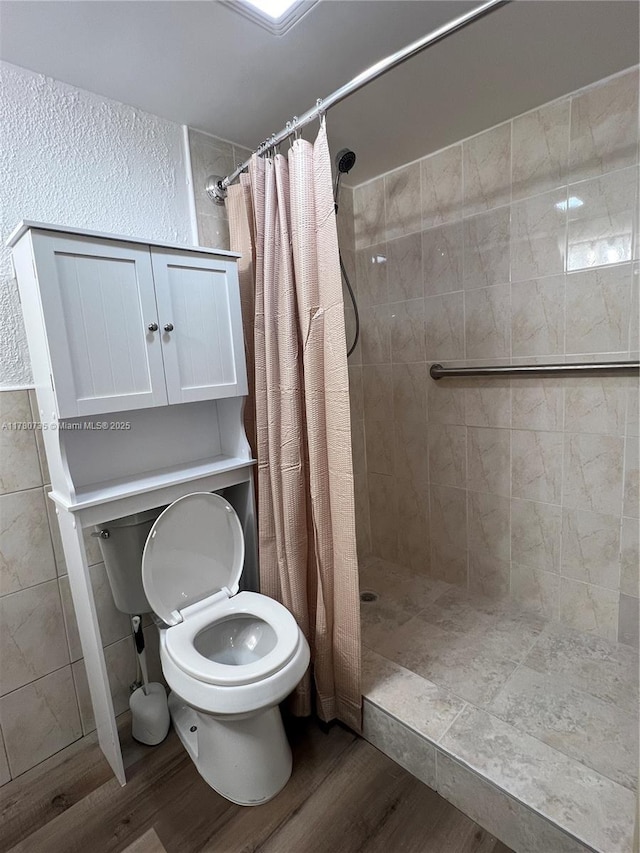 full bath featuring a tile shower, wood finished floors, and toilet
