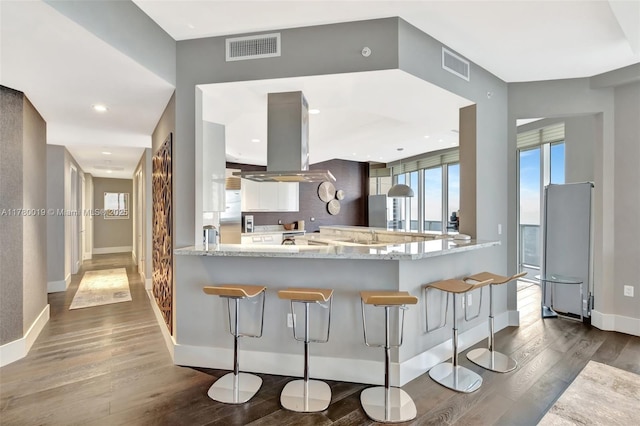 kitchen with freestanding refrigerator, a peninsula, visible vents, dark wood-style flooring, and island range hood