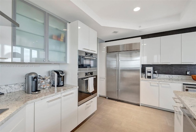 kitchen with a tray ceiling, appliances with stainless steel finishes, modern cabinets, and white cabinets