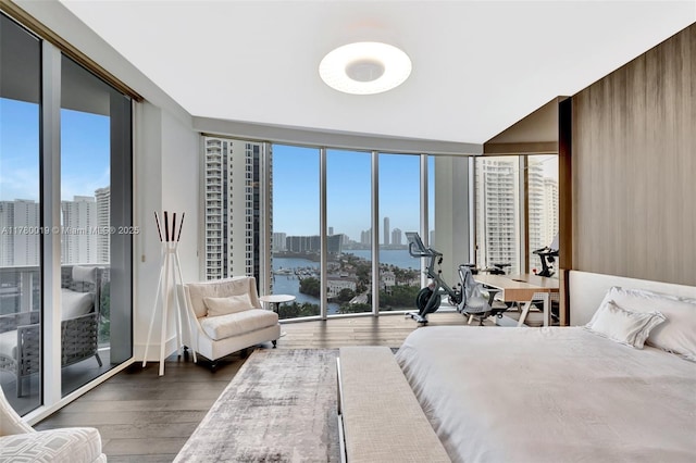 bedroom featuring wood finished floors, a view of city, floor to ceiling windows, and multiple windows