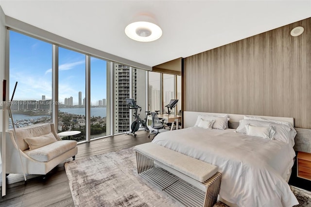 bedroom with wood finished floors, a view of city, and a wall of windows