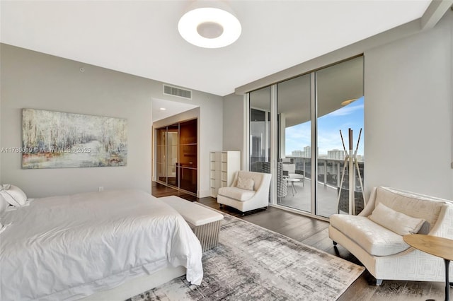 bedroom with floor to ceiling windows, visible vents, access to exterior, wood finished floors, and a view of city