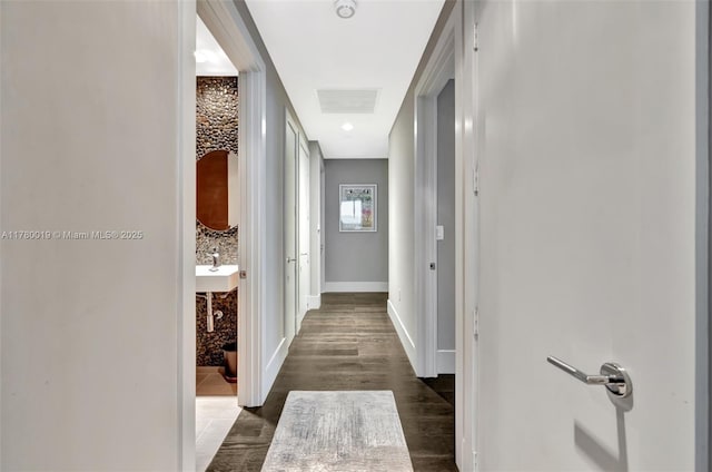 hall featuring dark wood-type flooring, baseboards, and a sink