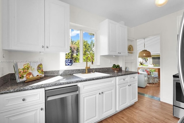 kitchen featuring light wood-style floors, white cabinetry, a sink, appliances with stainless steel finishes, and hanging light fixtures